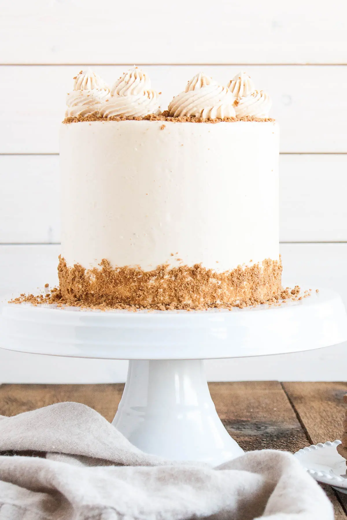 This Biscoff Cake pairs fluffy vanilla cake layers with a sweet cookie butter frosting and crushed speculoos cookies. | livforcake.com Straight on shot of the cake on a white cake stand and a white background.