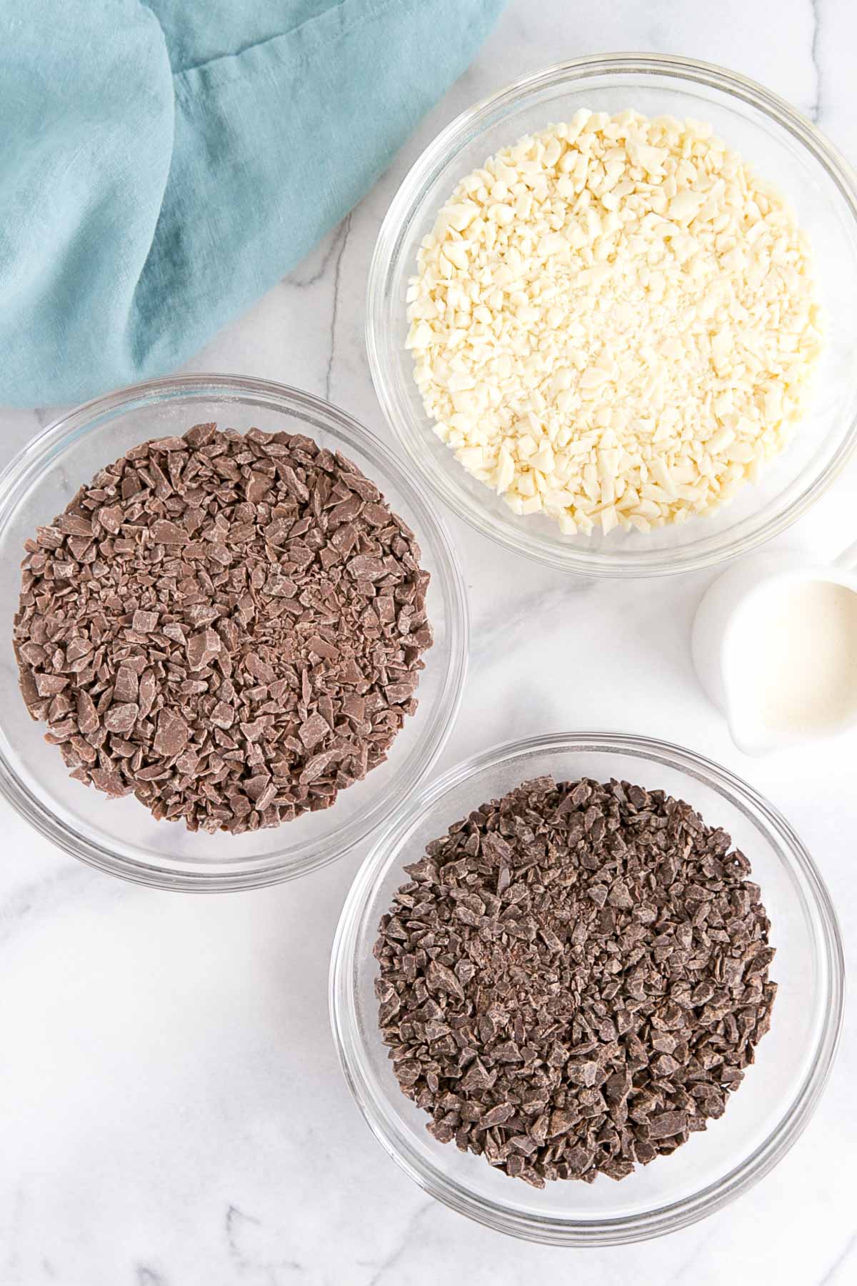 How to make Chocolate Ganache! A simple, two-ingredient recipe for a delicious frosting, filling, drip, or glaze. | livforcake.com Dark, milk, and white chocolate chopped up in separate bowls.