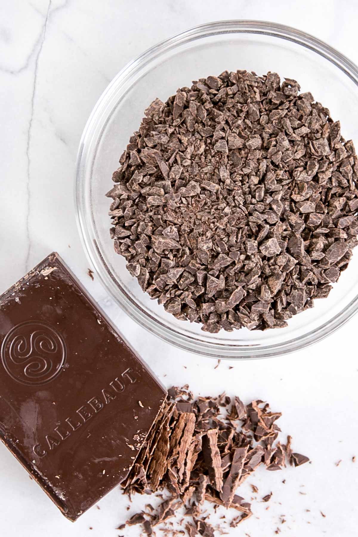How to make Chocolate Ganache! A simple, two-ingredient recipe for a delicious frosting, filling, drip, or glaze. | livforcake.com Dark chocolate chopped up in a glass bowl with a dark chocolate bar beside it.