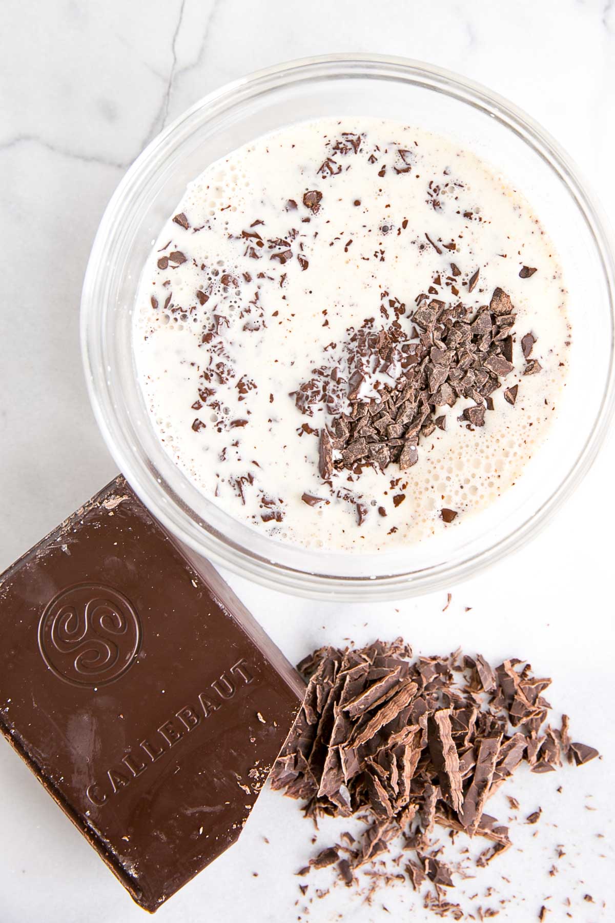 How to make Chocolate Ganache! A simple, two-ingredient recipe for a delicious frosting, filling, drip, or glaze. | livforcake.com Cream poured over chopped chocolate in a glass bowl.