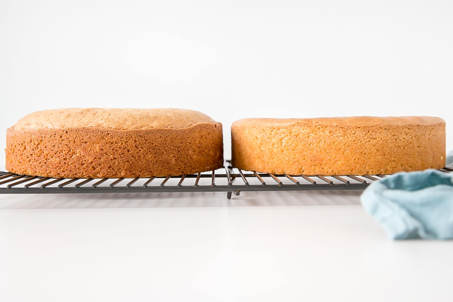 Learn how to bake flat cakes every single time! A simple tutorial on how to make sure your cakes come out nice and flat straight out of the oven. | livforcake.com Side-by-side shot of baked cakes on a cooling rack, one that is domed.