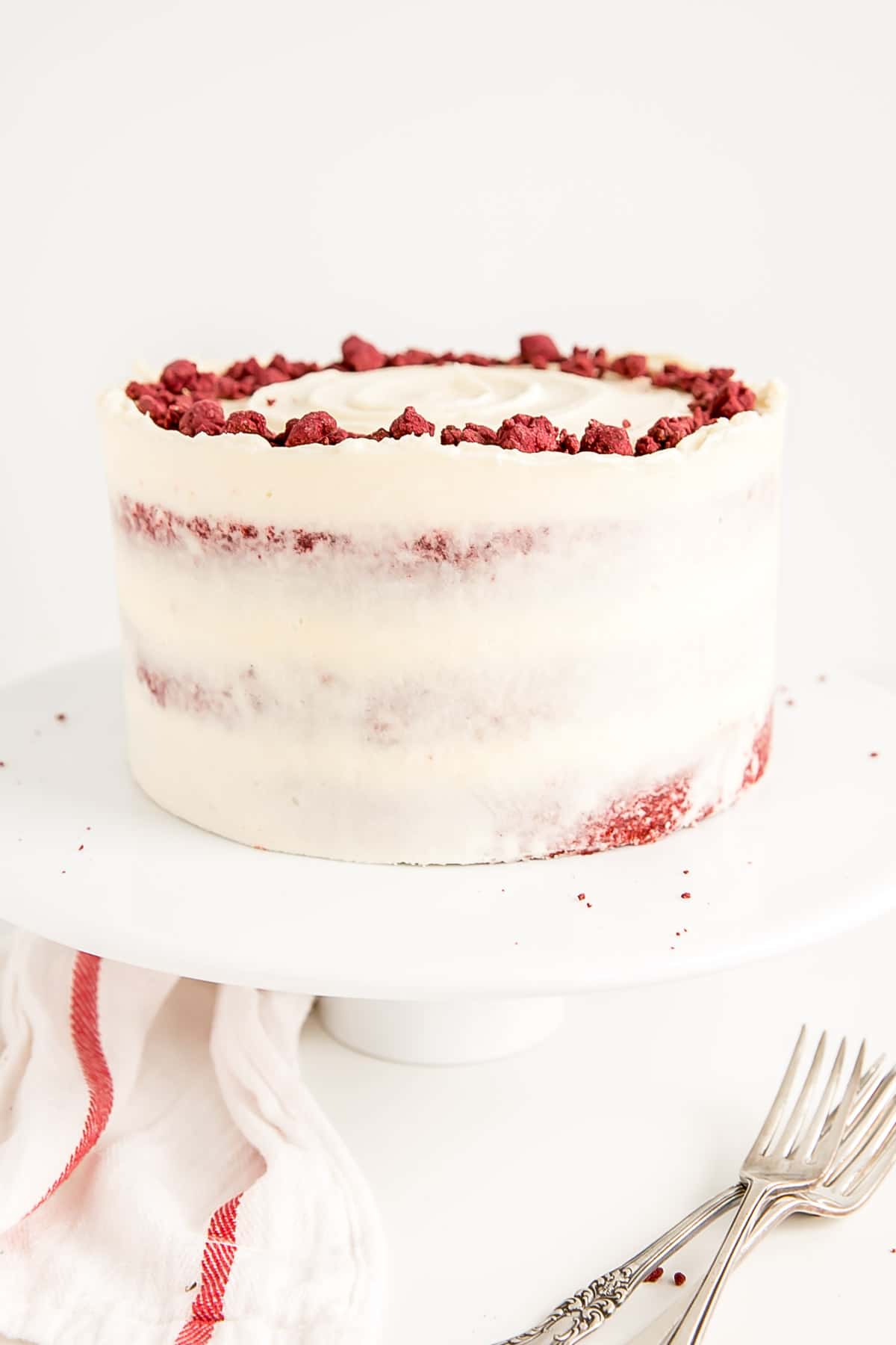 Classic Red Velvet Cake! Tender red cake layers with a hint of chocolate paired with a tangy cream cheese frosting and a red velvet crumble. | livforcake.com Angled shot of the cake on a cake stand.