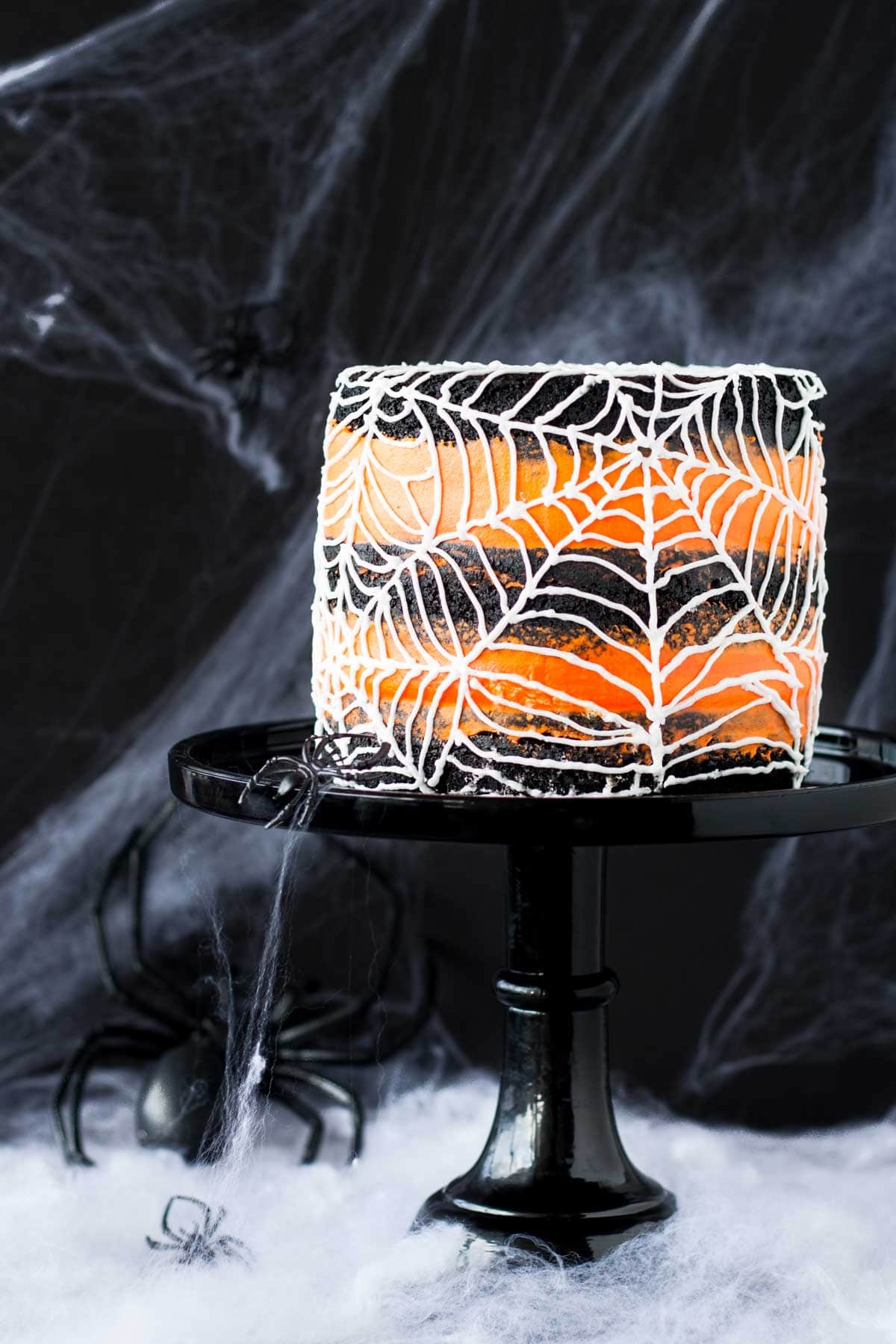 Naked cake with black cake layers and orange frosting decorated with piped spiderweb.